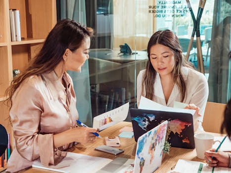 Two women collaborating in a business meeting, discussing ideas and reviewing documents.